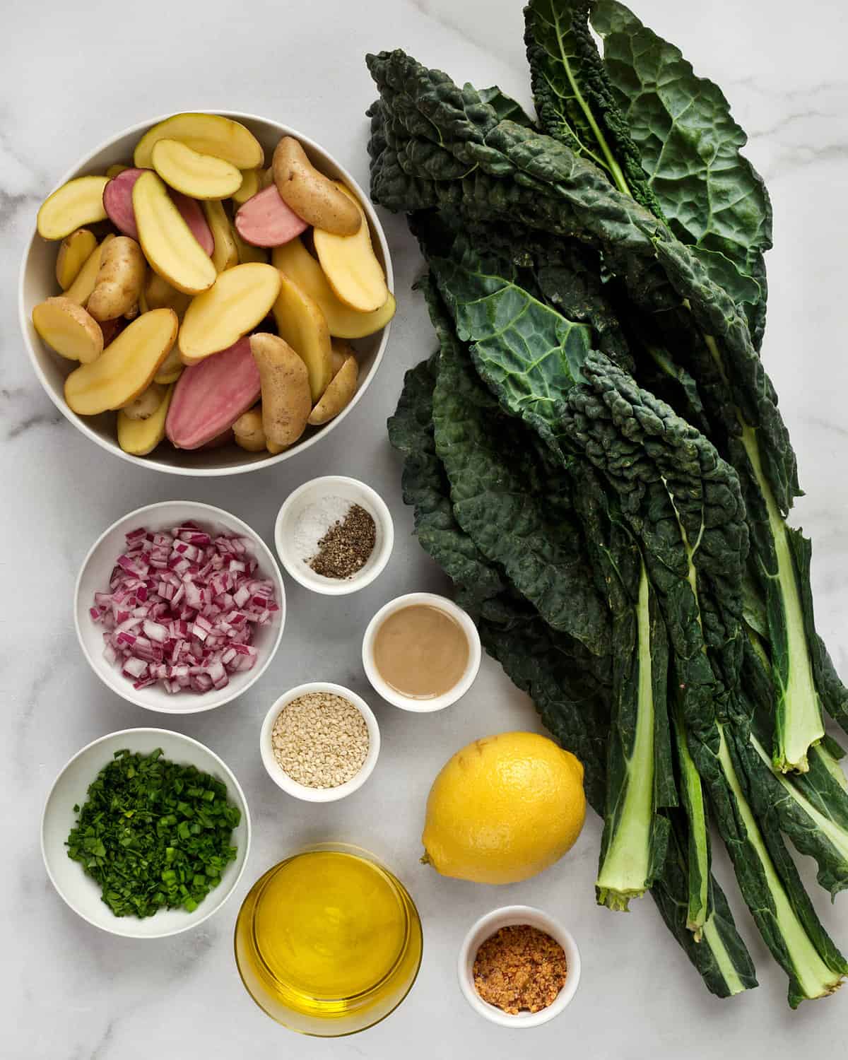 Ingredients including potatoes, kale, onions, herbs, olive oil, tahini, sesame seeds and onions.