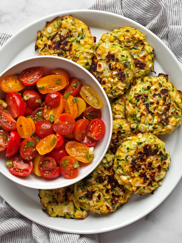 Baked zucchini corn fritters on a plate with a tomato salad.