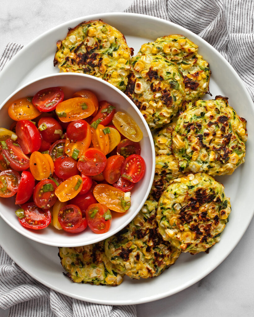 Baked zucchini corn fritters on a plate with a tomato salad.
