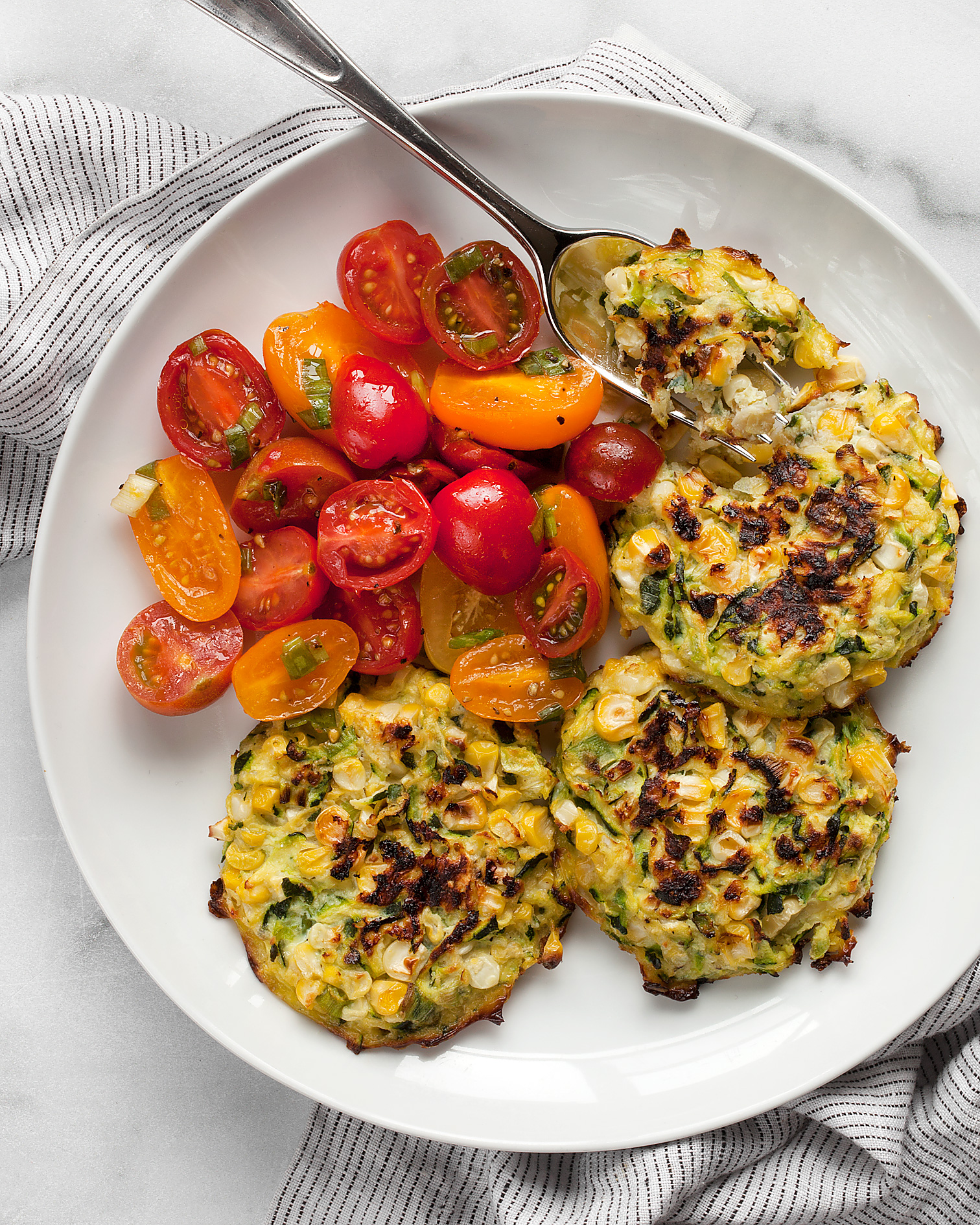 Baked zucchini corn fritters with a tomato salad on a plate with a fork.