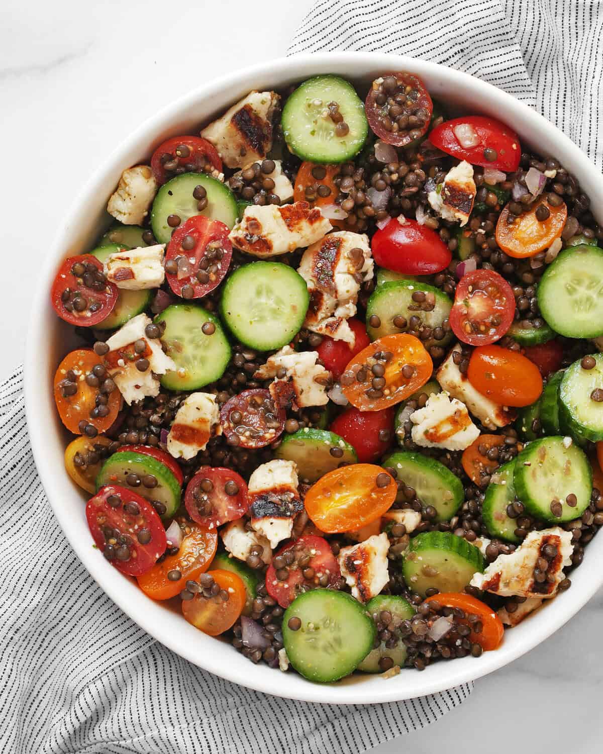Grilled halloumi salad with lentils, cucumbers and tomatoes in a large bowl.