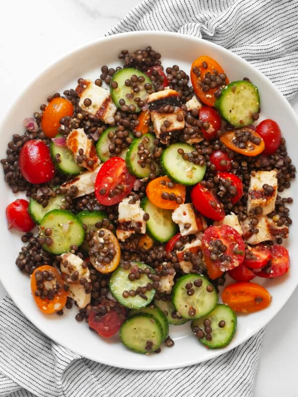 Grilled halloumi salad with lentils, cucumbers and tomatoes on a plate.