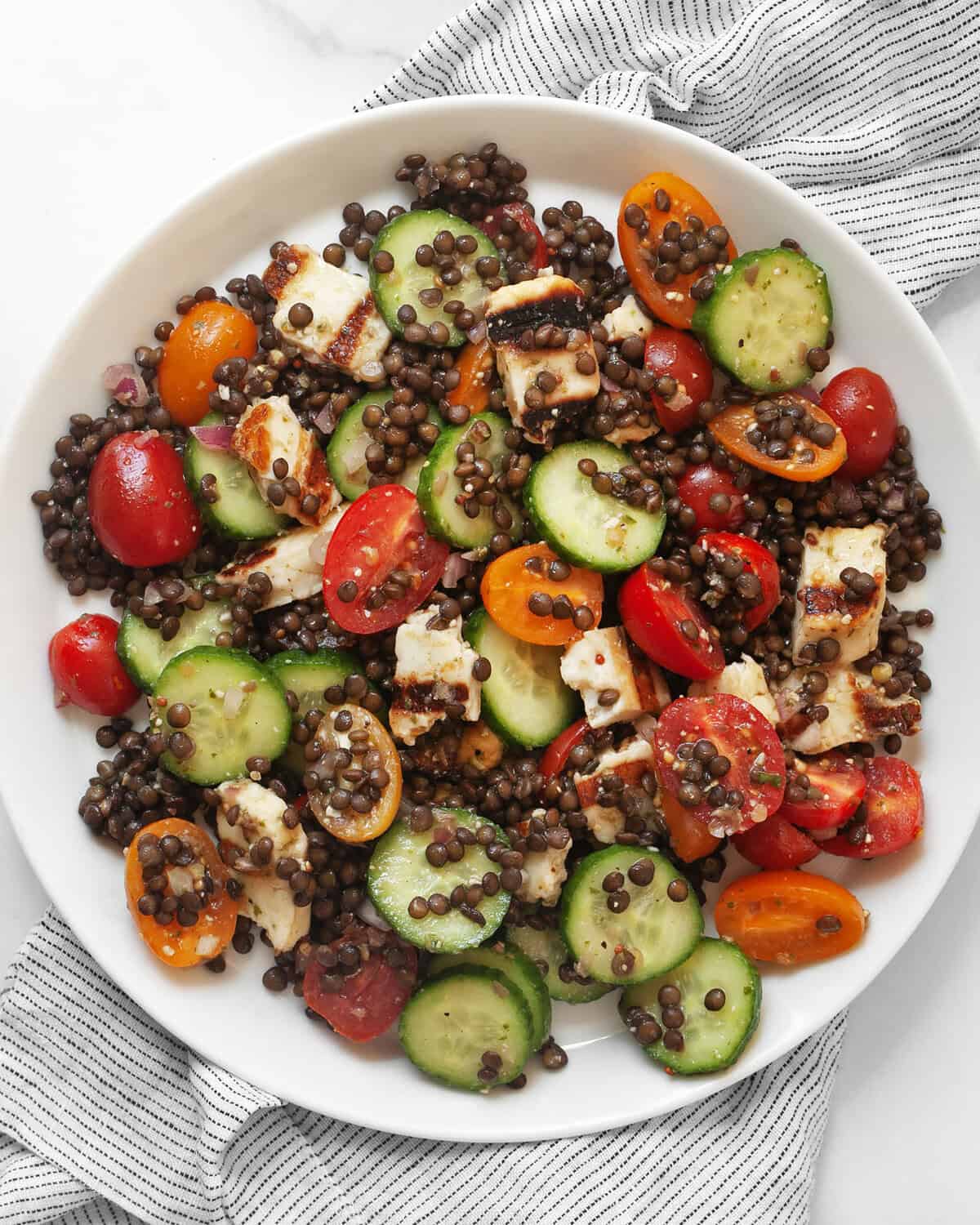 Grilled halloumi salad with lentils, cucumbers and tomatoes on a plate.