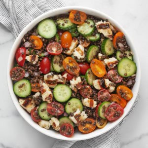 Lentil salad with grilled halloumi, cucumbers and tomatoes in a large bowl.