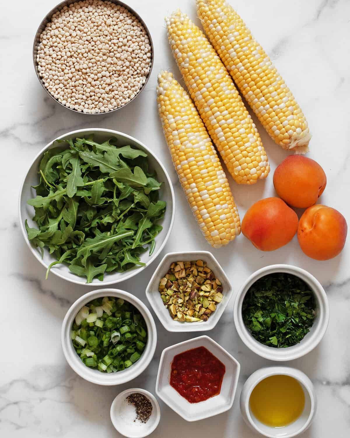 Ingredients including corn, apricots. couscous, harissa, pistachios, scallions, parsley, salt and pepper.