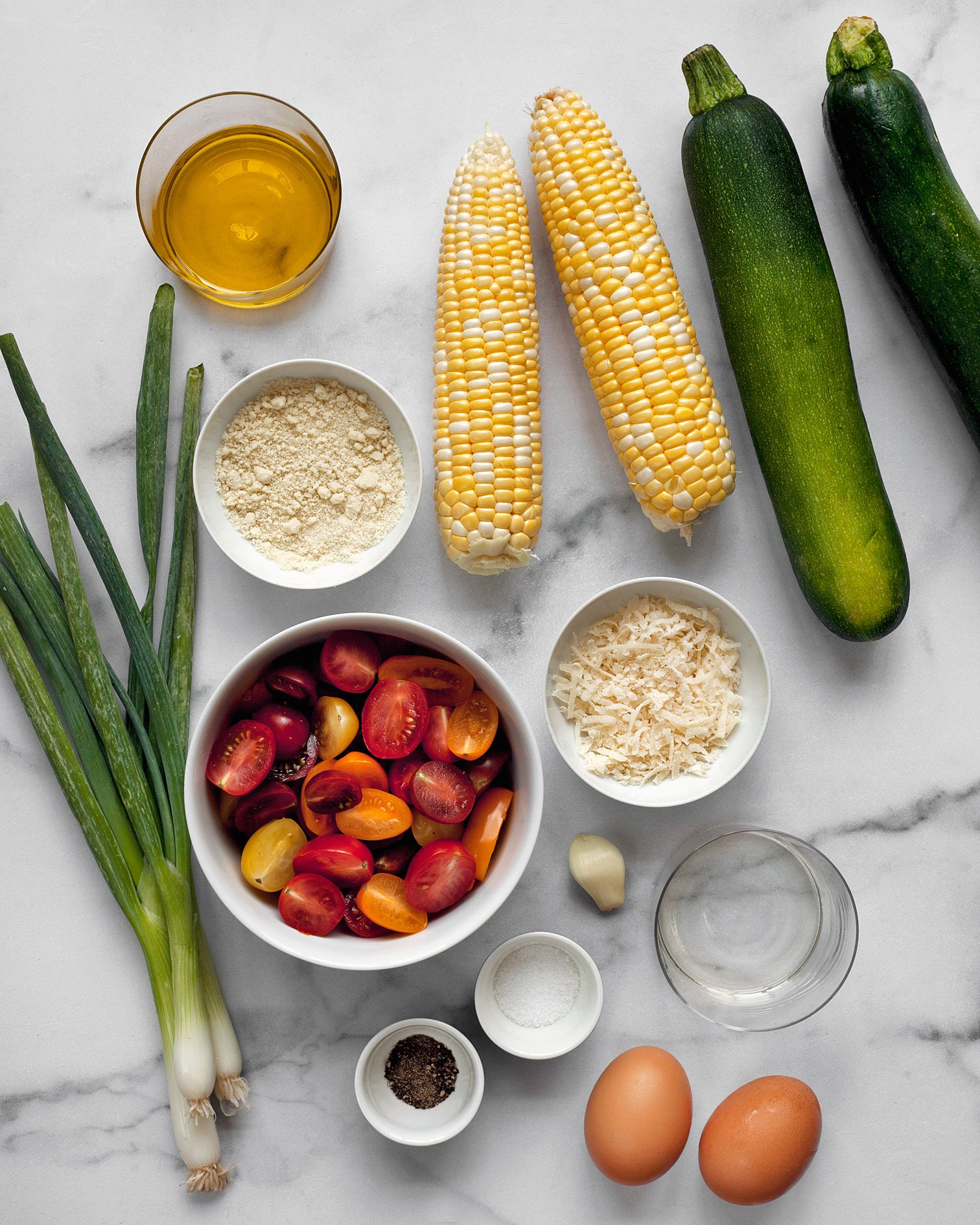 Ingredients including zucchini, corn, parmesan, scallions, tomatoes and olive oil