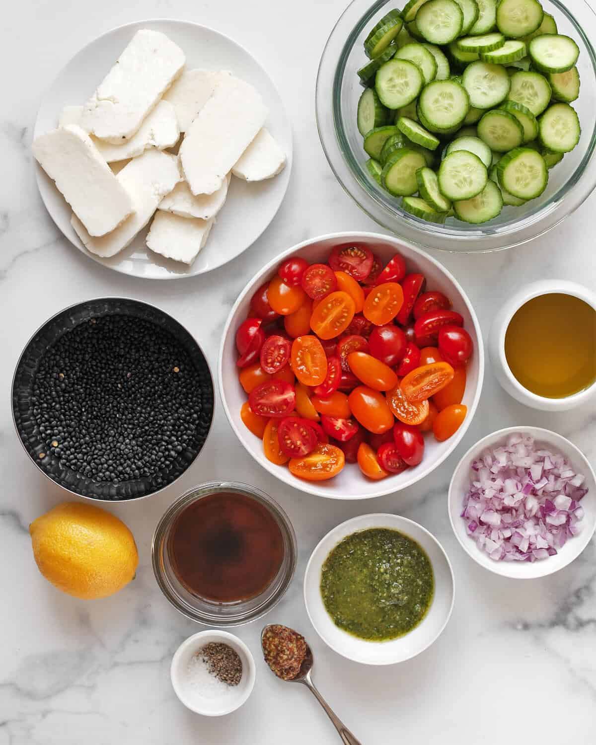 Ingredients including halloumi, black lentils, tomatoes, cucumbers, red onions, pesto, olive oil, salt, pepper, lemon, red wine vinegar and mustard.