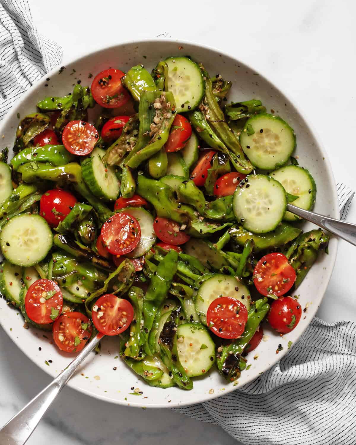 Grilled shishito pepper cucumber salad in a bowl with 2 spoons.