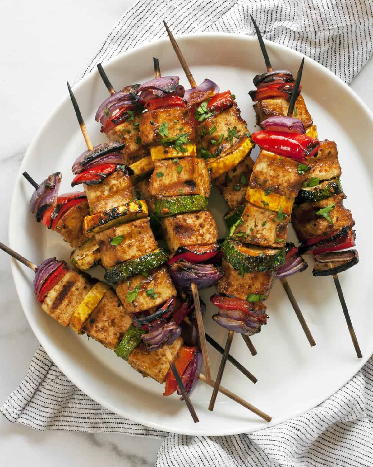 BBQ tofu veggie skewers stacked on a plate.