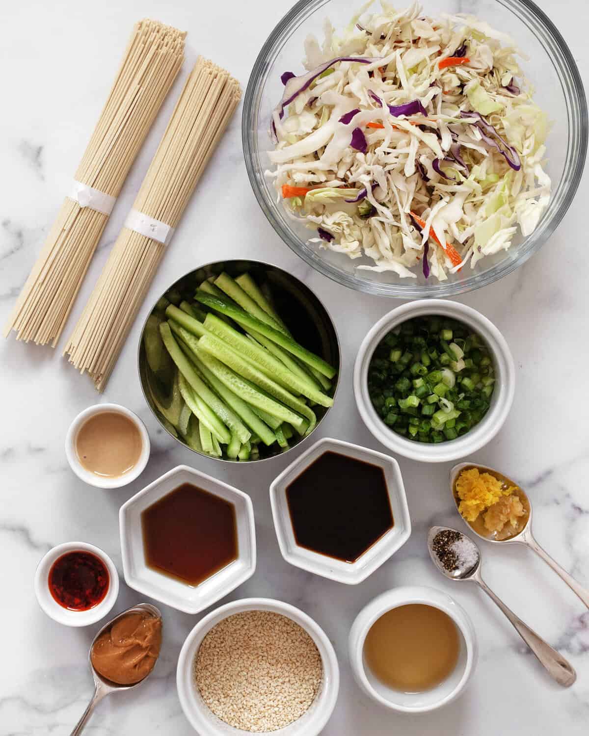 Ingredients including egg noodles, coleslaw mix, cucumbers, scallions, garlic, ginger, peanut butter, tahini, sesame seeds, soy sauce, rice vinegar and sesame oil.