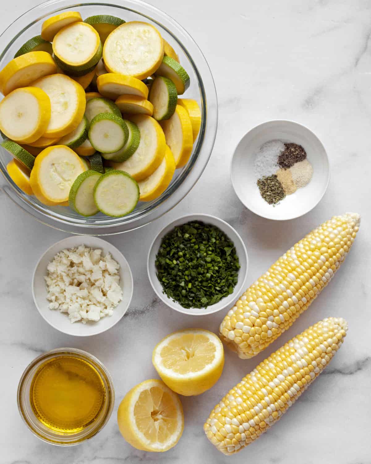 Ingredients including zucchini, yellow squash, corn, spices, feta, olive oil and fresh herbs.