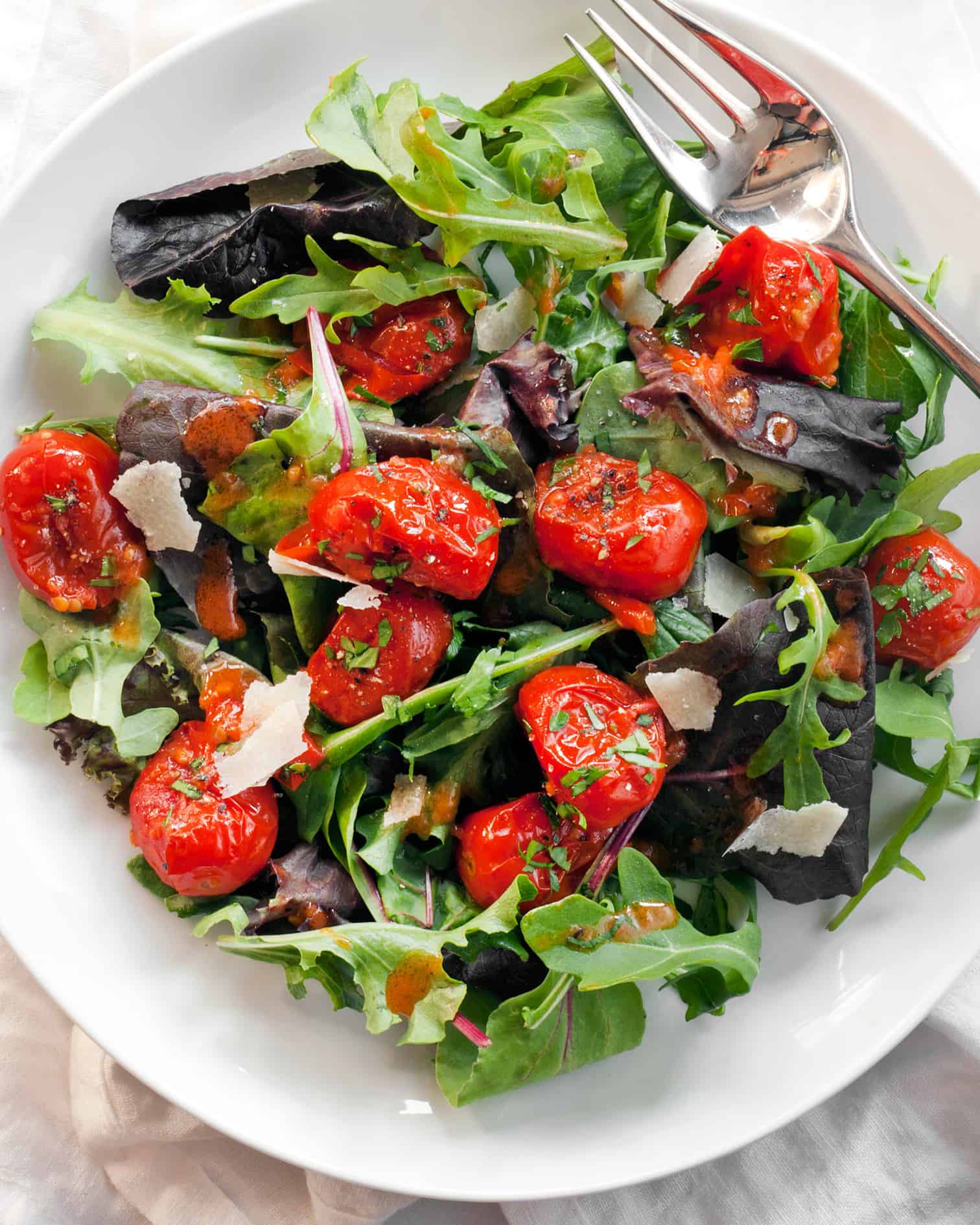 Mixed greens salad with tomato vinaigrette on a plate.