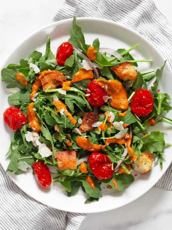Arugula salad with roasted tomato vinaigrette drizzled on it.