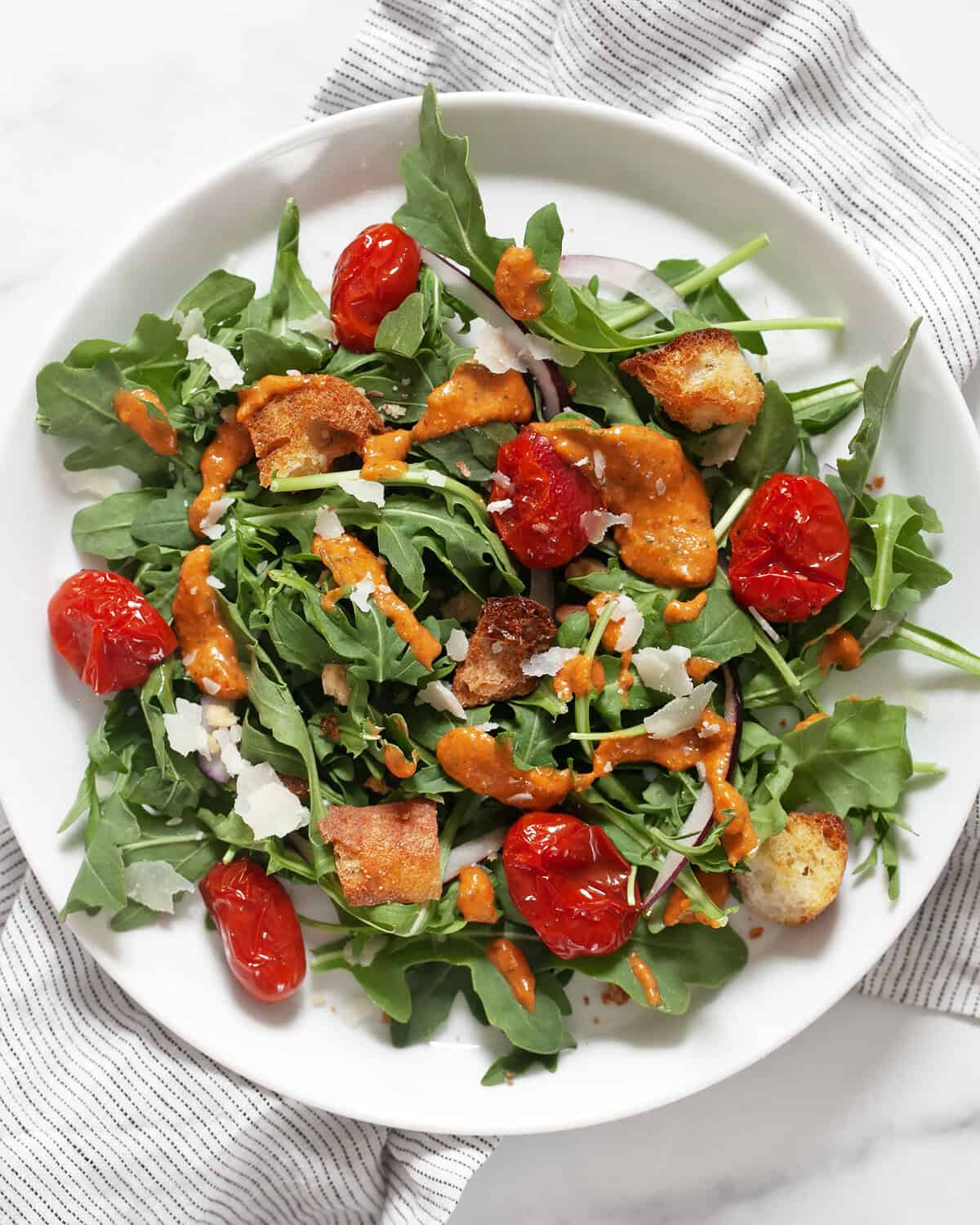 Arugula salad with roasted tomato vinaigrette drizzled on it.