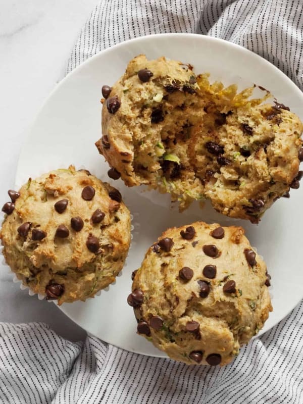 Three chocolate chip zucchini muffins on a plate with one torn in half.