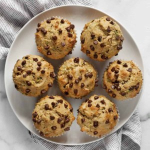 Seven chocolate chip zucchini muffins on a plate.