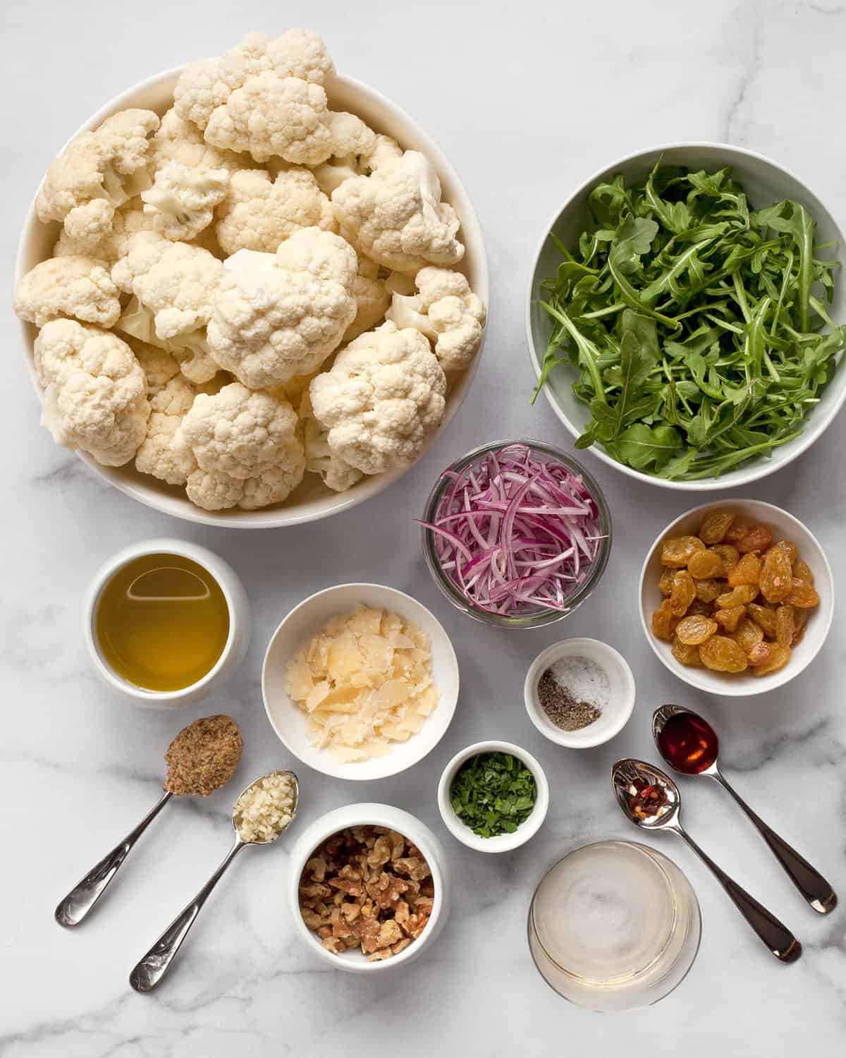Ingredients including cauliflower, arugula, red onions, Parmesan, raisins, olive oil and vinegar.