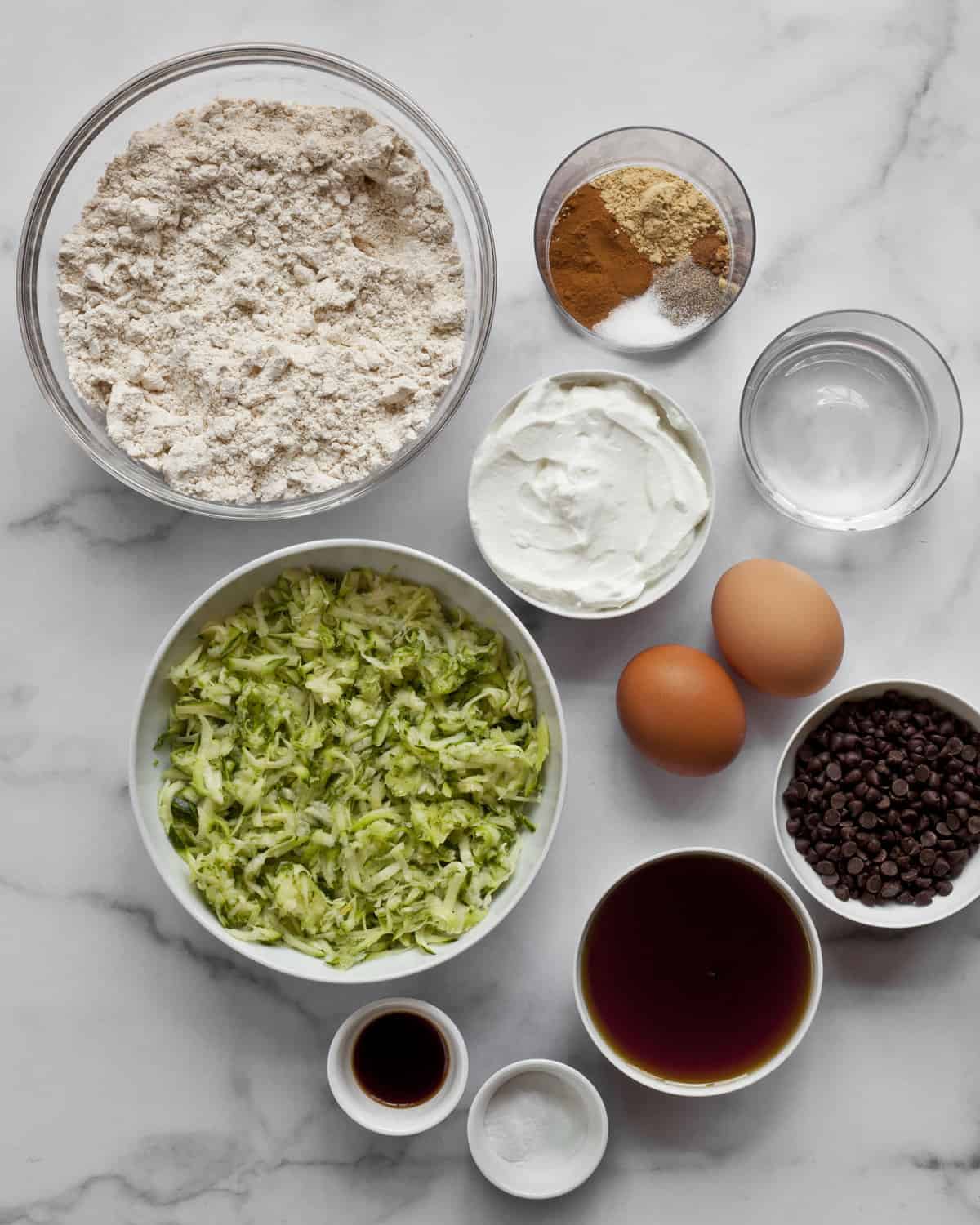 Ingredients including flour, shredded zucchini, eggs, vanilla extract, yogurt and spices.