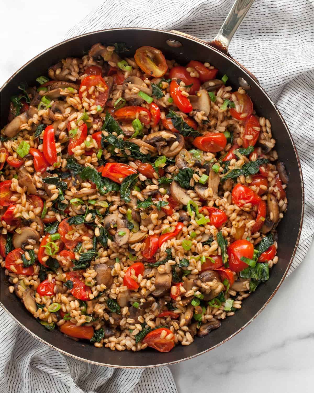 Mushroom farro with tomatoes and kale in a skillet.