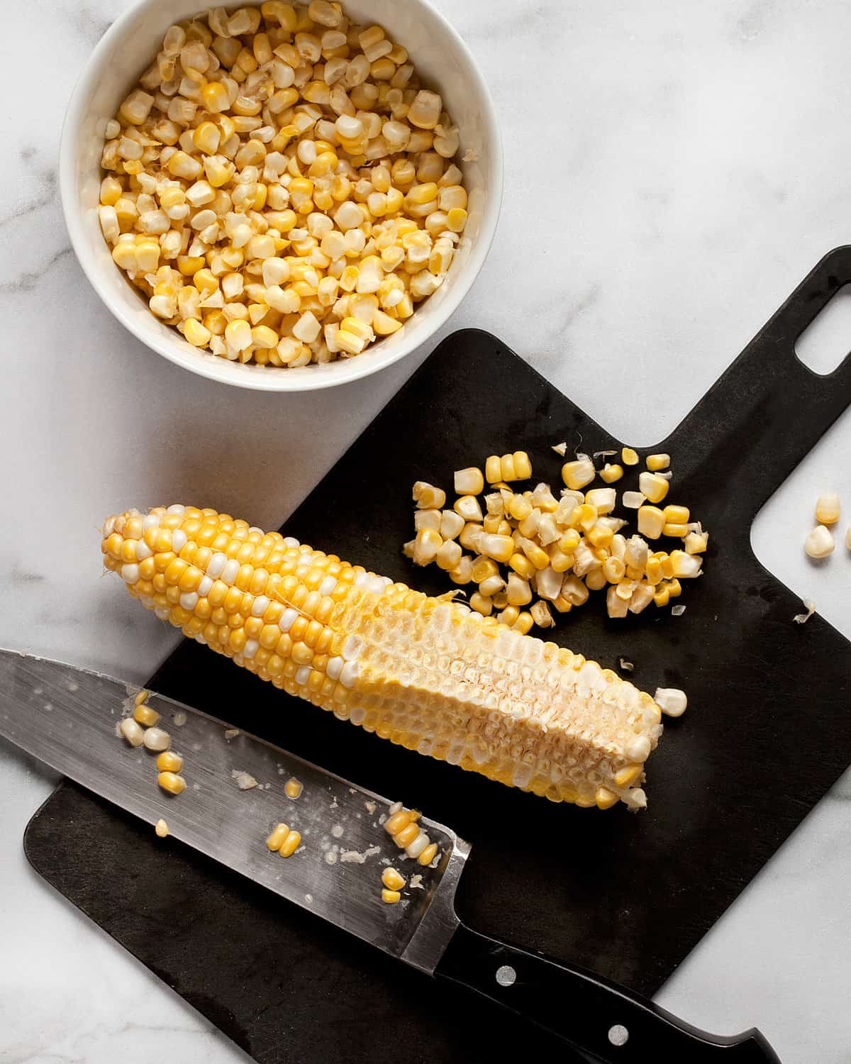 Knife on cutting board with ear of corn and knife.