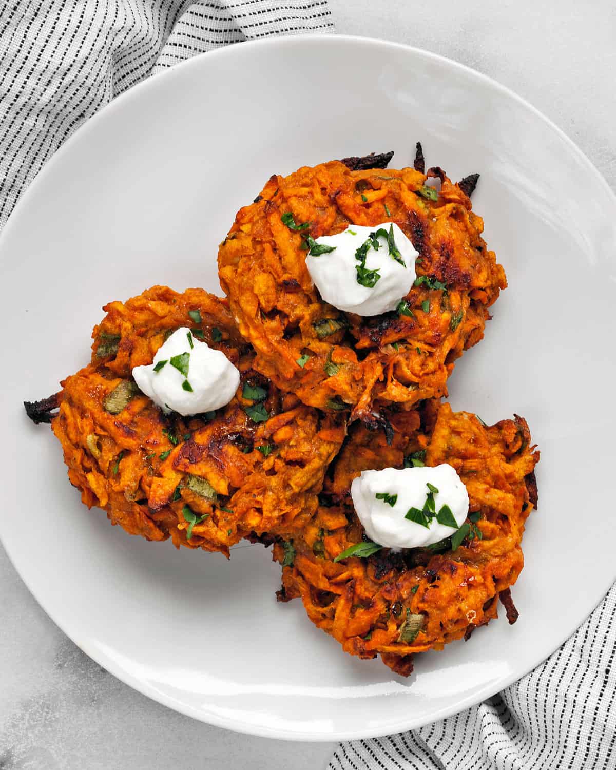 Three sweet potato fritters topped with a dollop of Greek yogurt and chopped parsley.