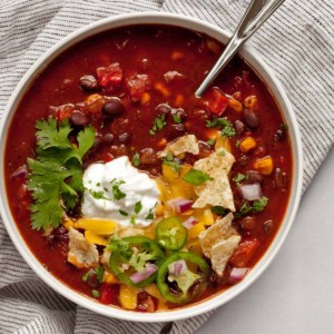 Bowl of black bean chili with tortilla chips, sour cream, cilantro and cheese.