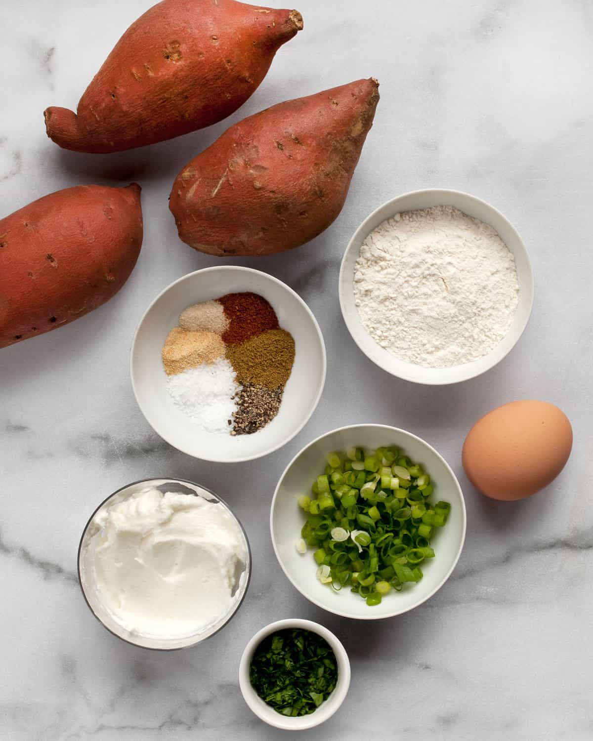 Ingredients including sweet potatoes, spices, flour, egg and scallions.