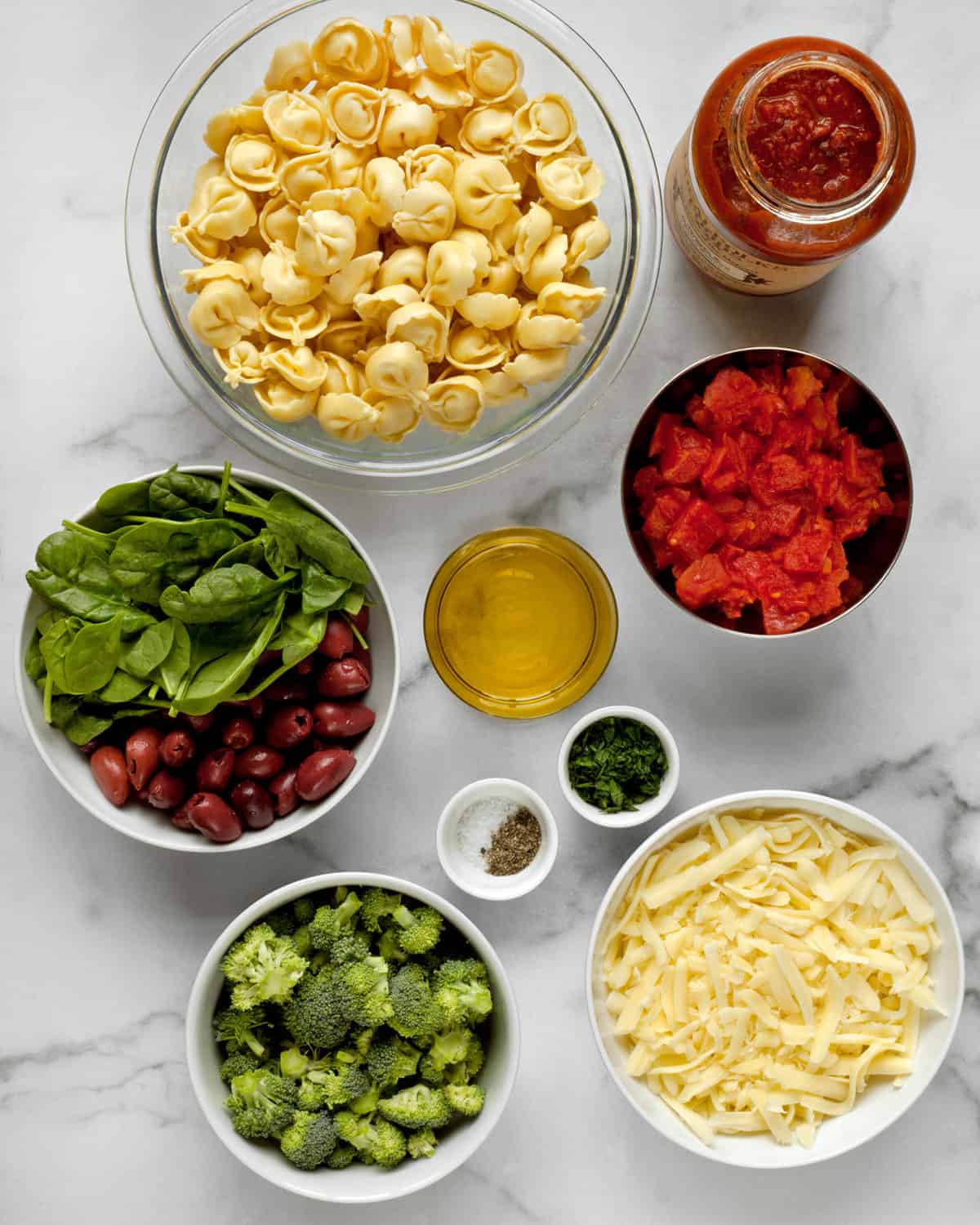 Ingredients including tortellini, olives, spinach, tomatoes, cheese, olive oil and broccoli.
