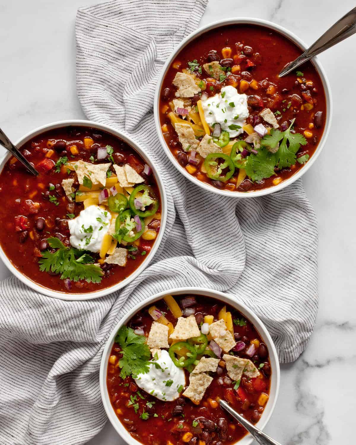 Three bowls of chili with toppings.