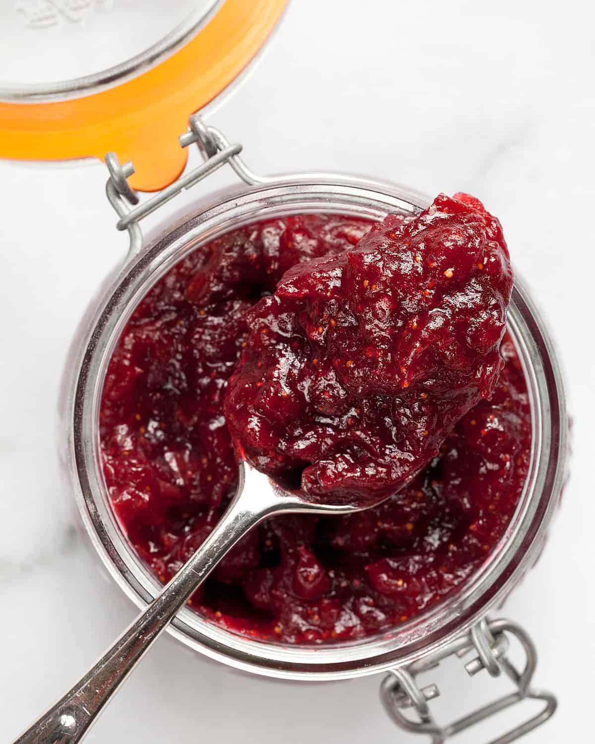 Spoon with cranberry jam sitting on a jar.