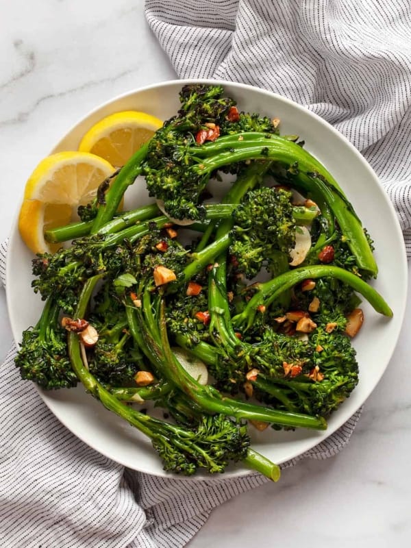 Sauteed broccolini piled on a plate with lemon wedges on the side.