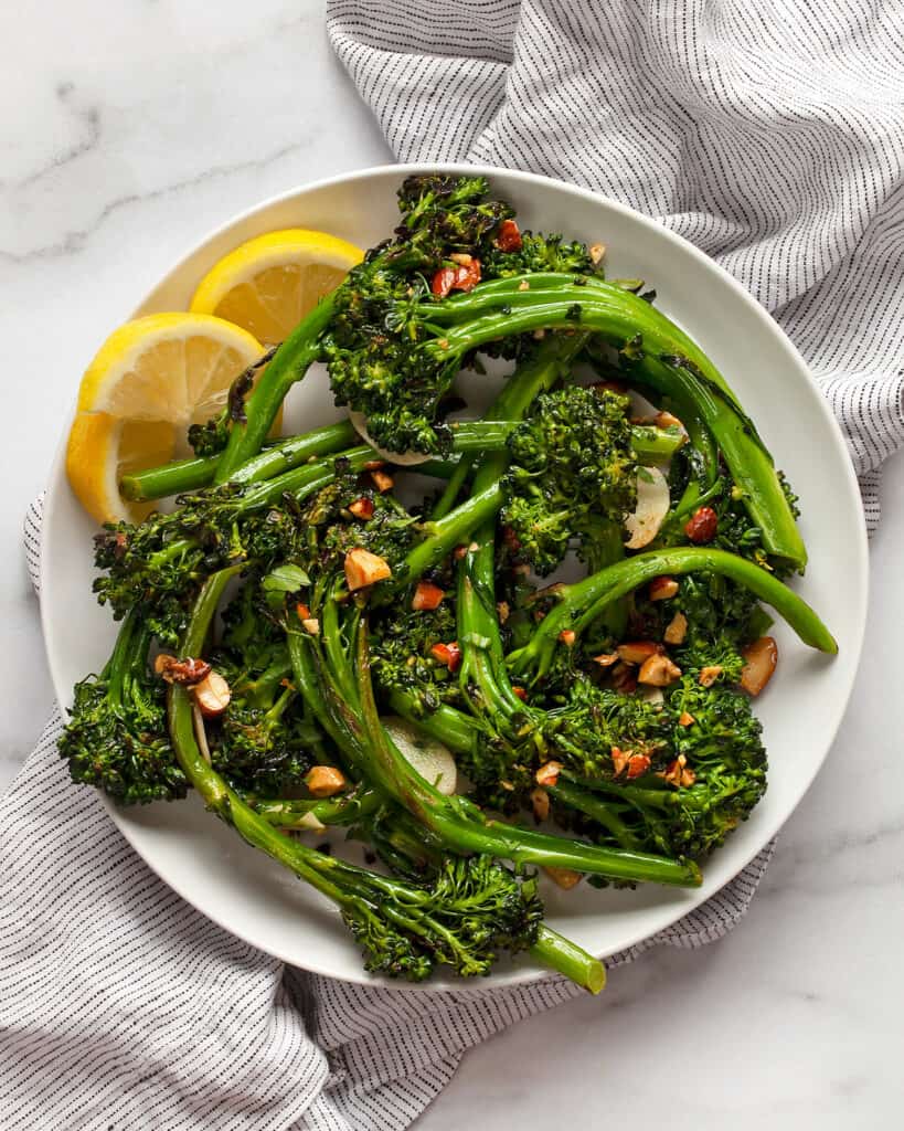 Sauteed broccolini piled on a plate with lemon wedges on the side.