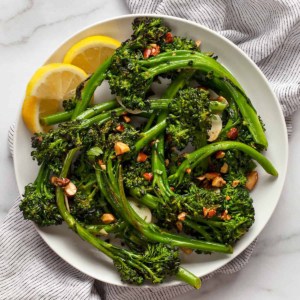 Sauteed broccolini piled on a plate with lemon wedges.
