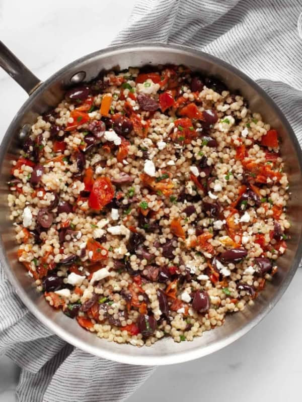 Pearl couscous with tomatoes and olives in a skillet.