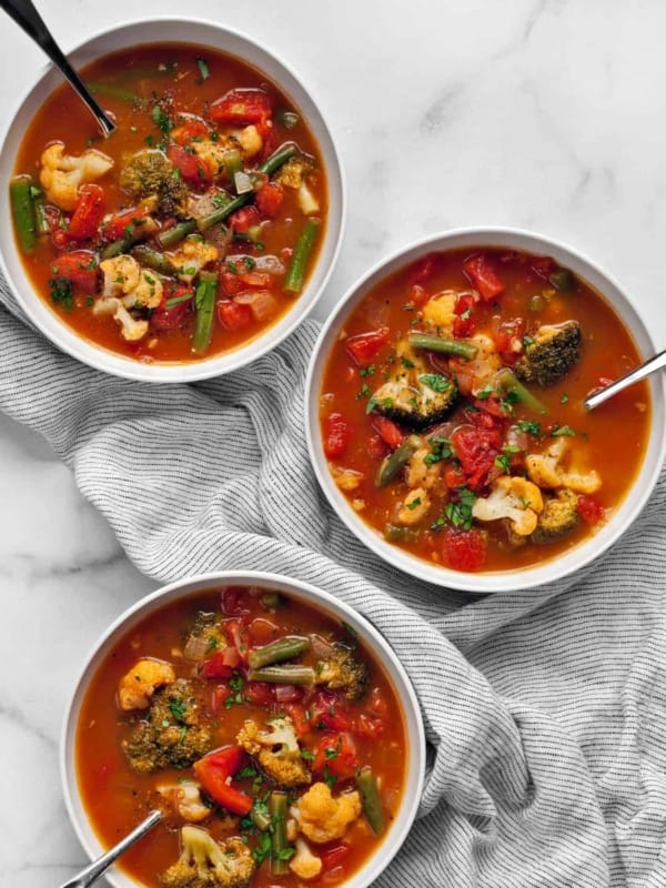 Three bowls of vegetable soup on a striped napkin.