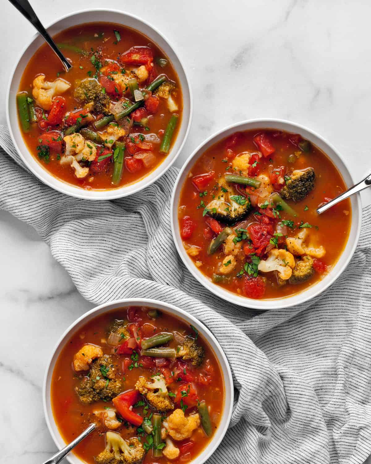 Three bowls of vegetable soup on a striped napkin.