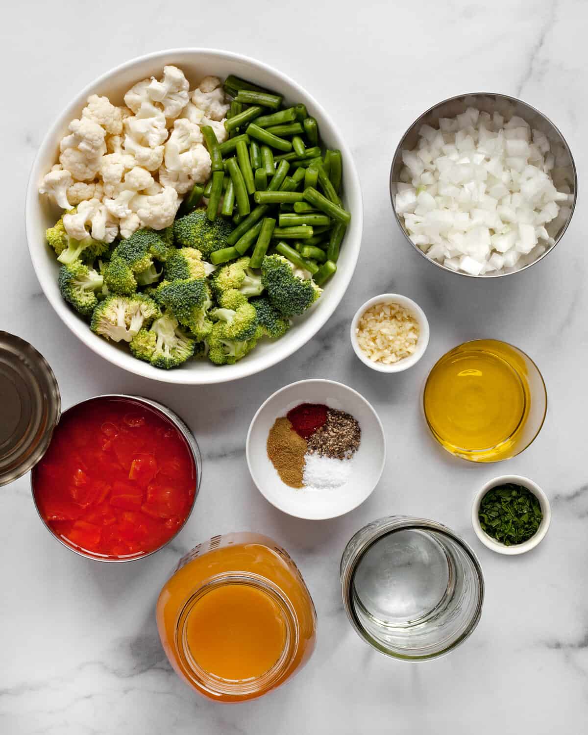 Ingredients including broccoli, cauliflower, green beans, canned tomatoes, onions, garlic, spices, olive oil and broth.
