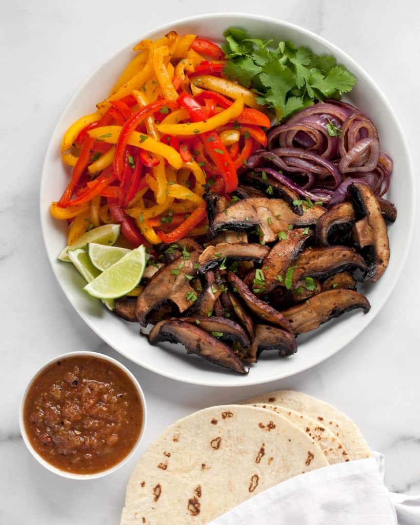 Roasted mushrooms, peppers and onions on a plate with salsa and tortillas