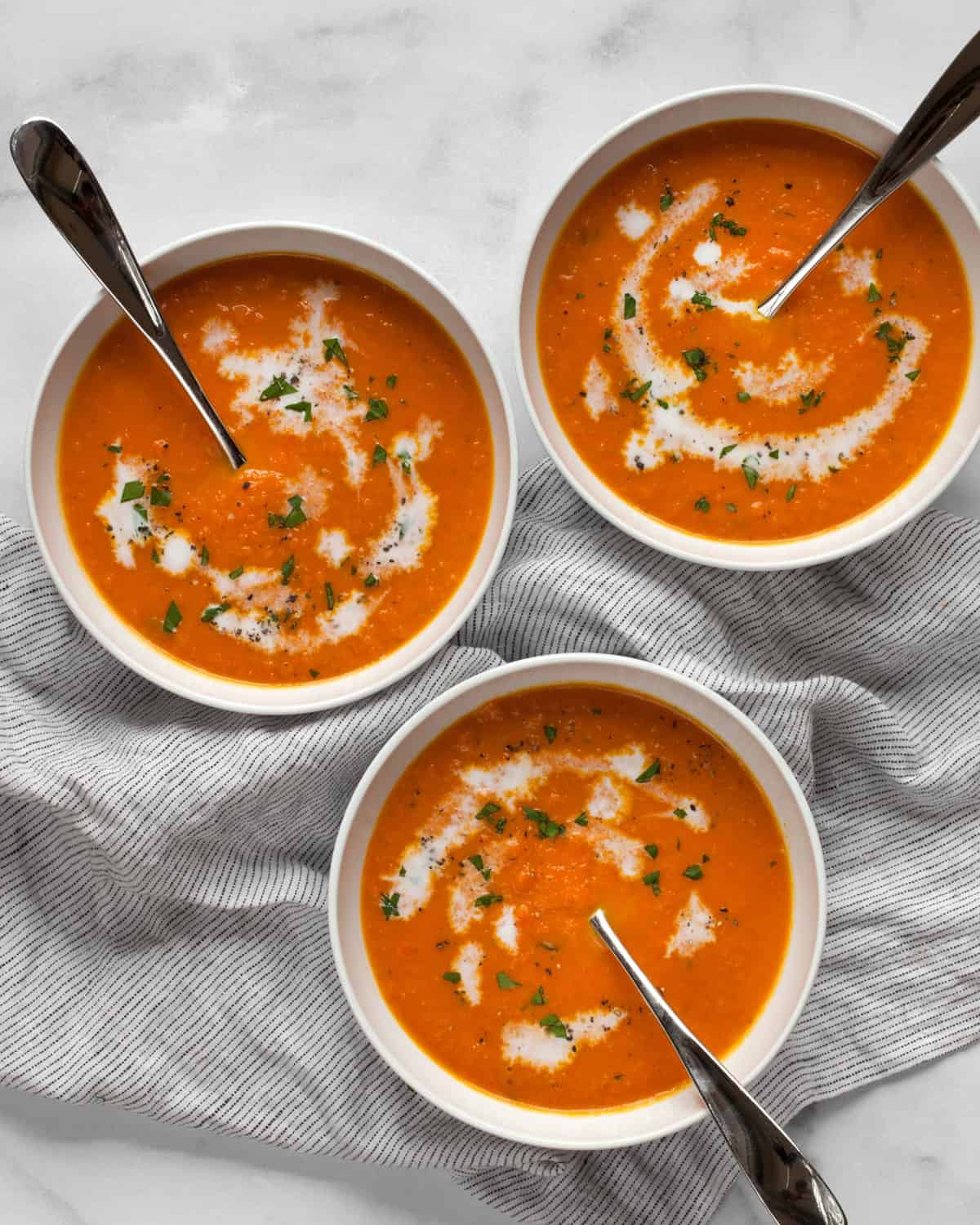 Three bowls of carrot ginger soup topped with coconut milk and parsley.