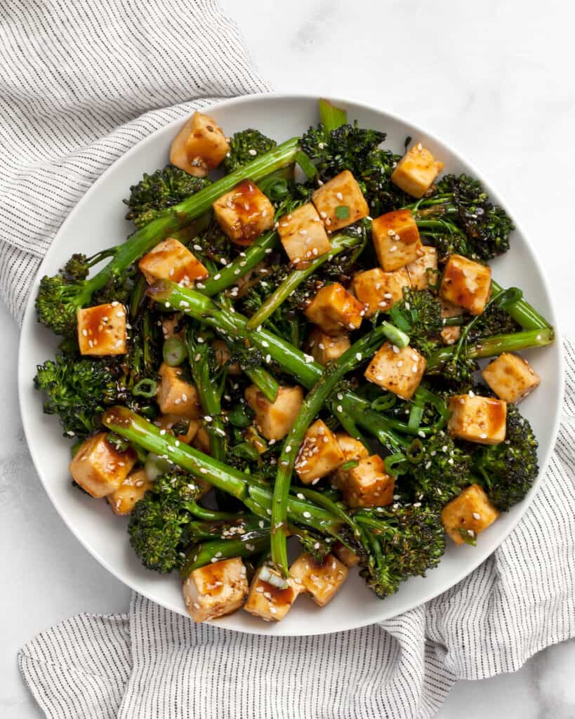 Baked tofu and broccolini with teriyaki sauce on plate.