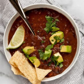 Bowl of black bean soup with avocados and tortilla chips.