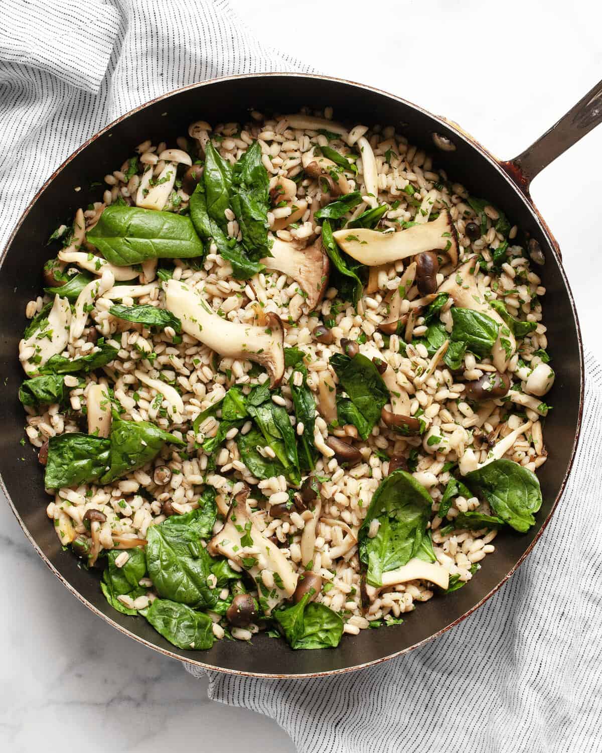 A skillet with barley, sautéed mushrooms and spinach.