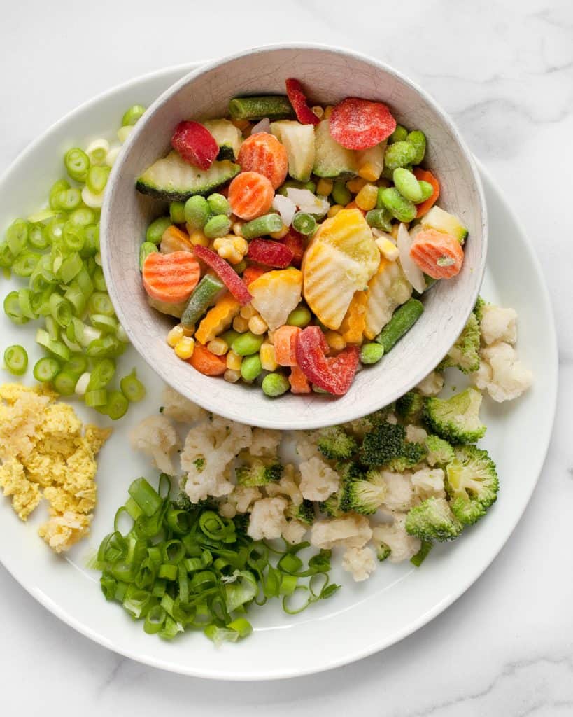 Frozen vegetables on a plate with sliced scallions and minced ginger and garlic