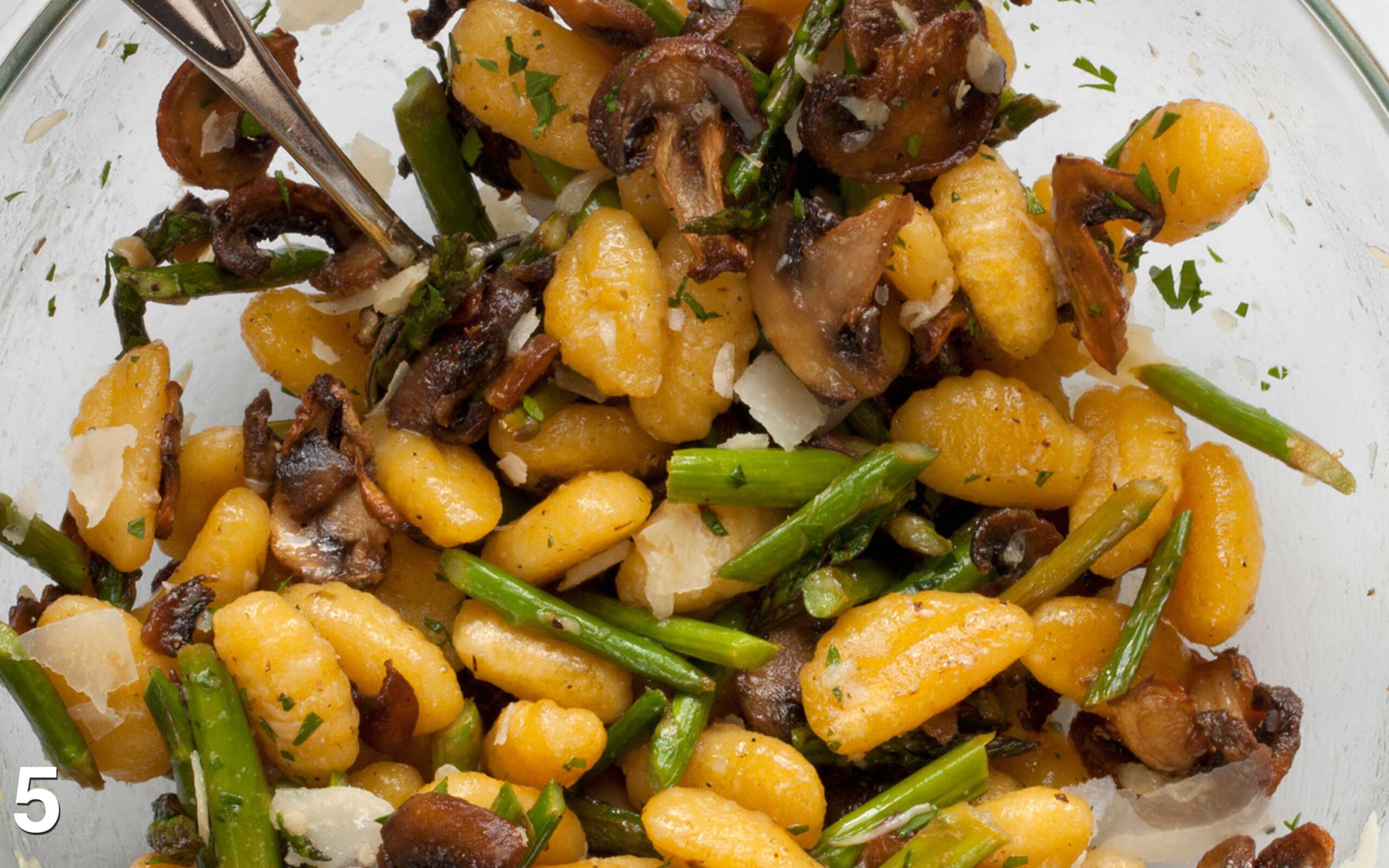 Parsley and Parmesan stirred into gnocchi and vegetables in a bowl.