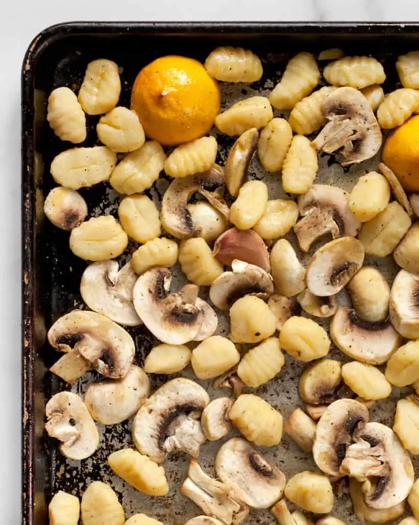 Gnocchi, mushrooms and halved lemons on a sheet pan