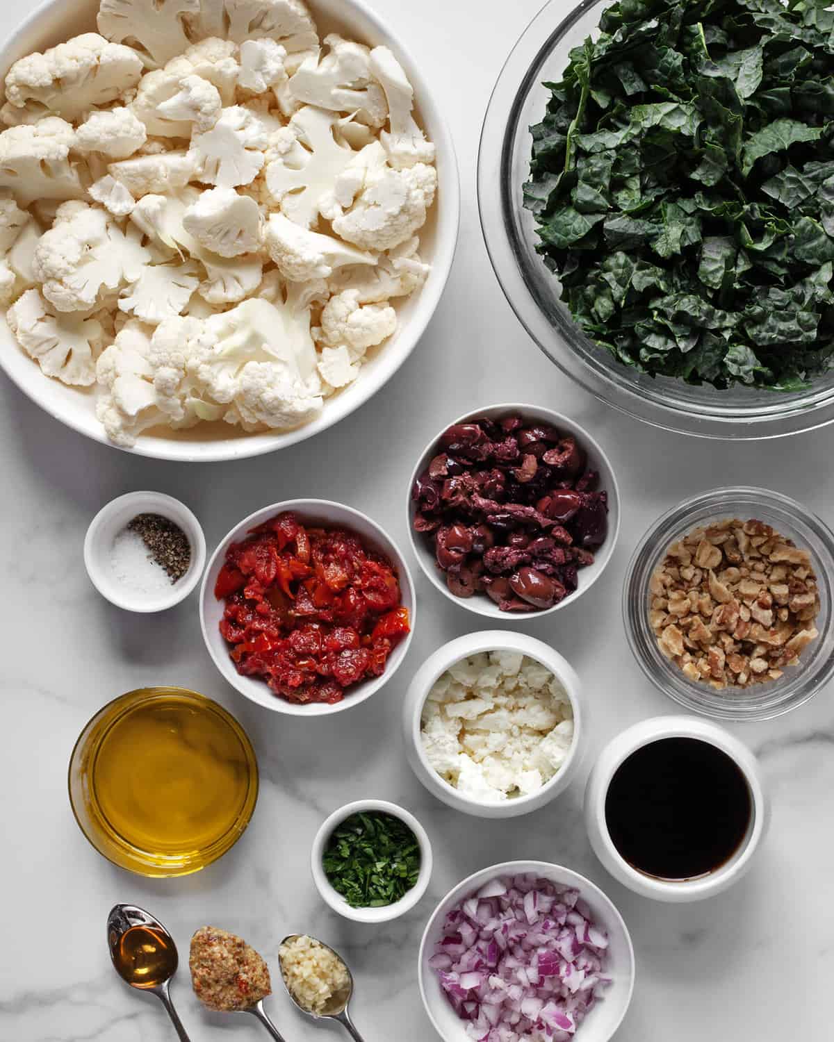 Ingredients including cauliflower, tomatoes, onions, olives, feta, walnuts, parsley, mustard, balsamic vinegar, olive oil, salt and pepper.