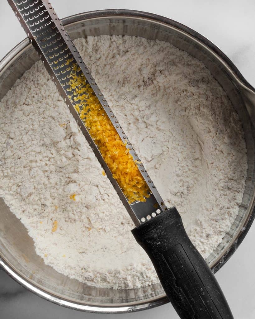 Adding lemon zest to the dry ingredients in a bowl