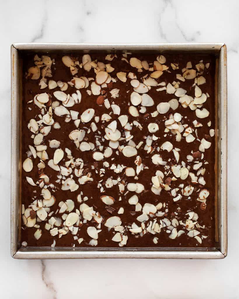 Chocolate cake batter in a square pan topped with almonds