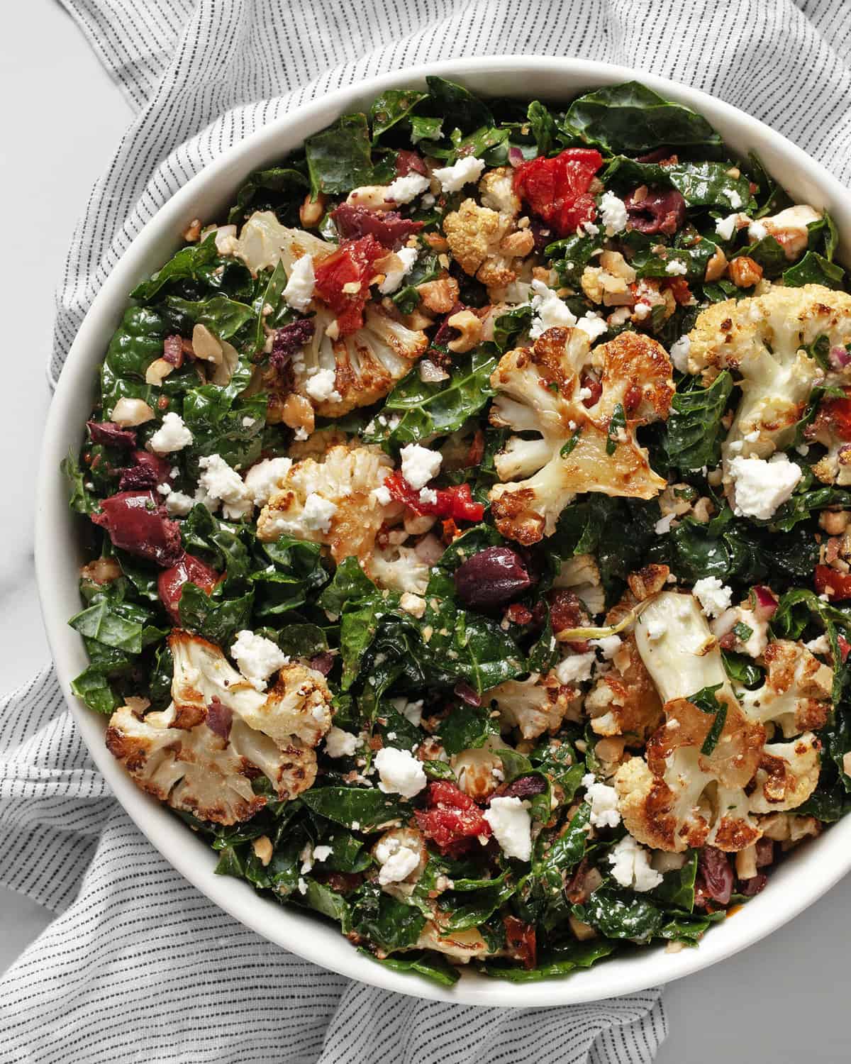 Cauliflower kale salad with tomatoes and olives in a bowl.