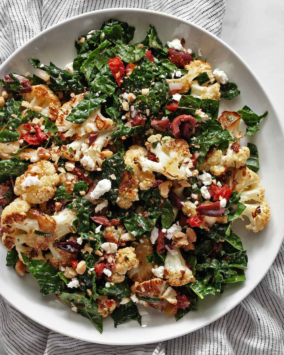 Roasted cauliflower kale salad with tomatoes and olives on a plate.